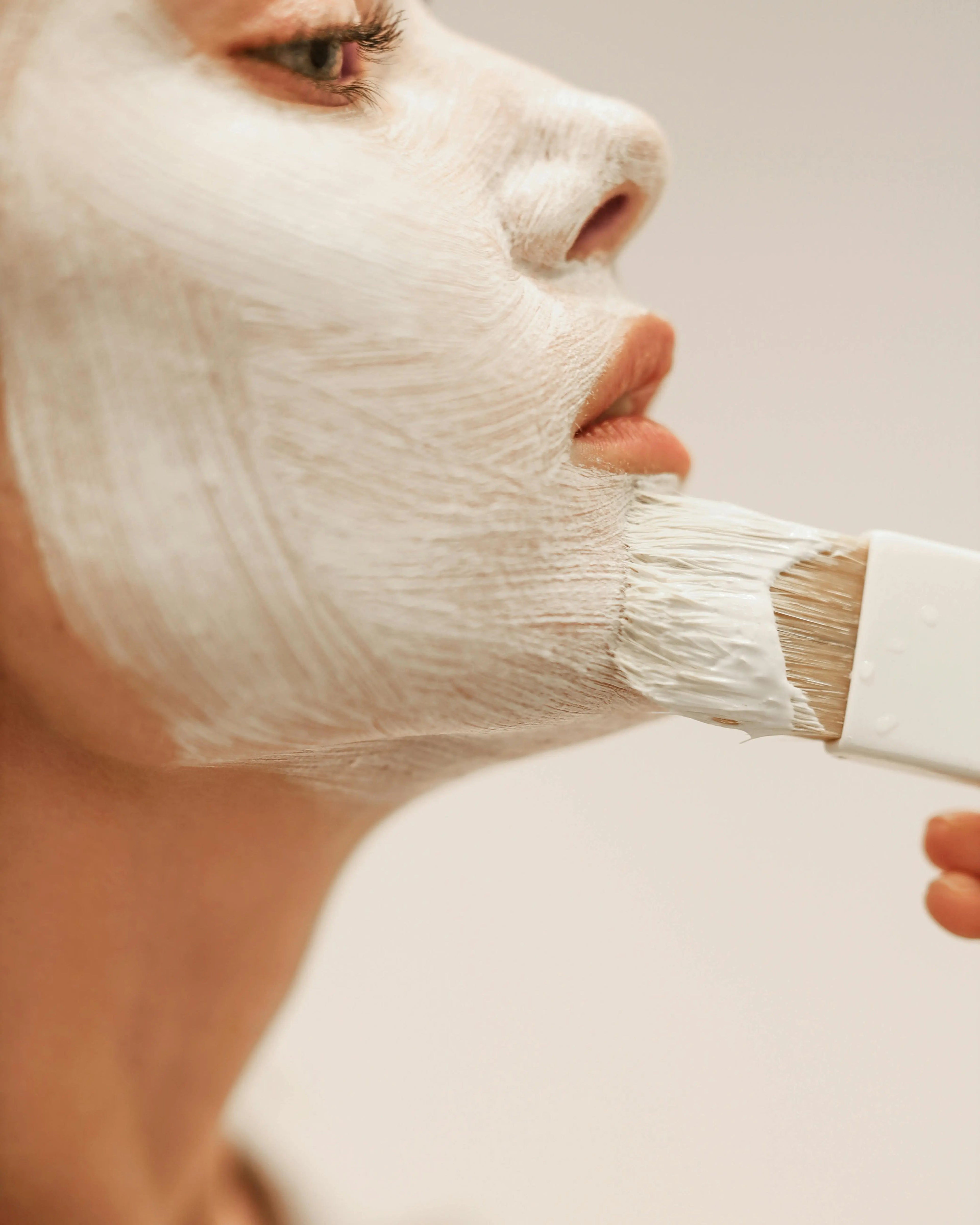 Mujer con mascarilla facial blanca, lista para tratamientos de belleza que rejuvenecen y cuidan la piel.
